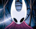 A screencap of Hollow Knight: Silksong's opening cutscene. A close-up shot of protagonist Hornet moments before she breaks out of a metal cage. Her curved white mask and red cloak are lit up as a glowing strand of silk surrounds her.