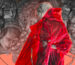 A screenshot of Zero Parades key art from the September 2025 Sony State of Play gameplay trailer. A short-haired woman in a bright red trench coat looks toward the viewer. A collage of gloomy black and white heads surround her with an orange background peeking through at the bottom.